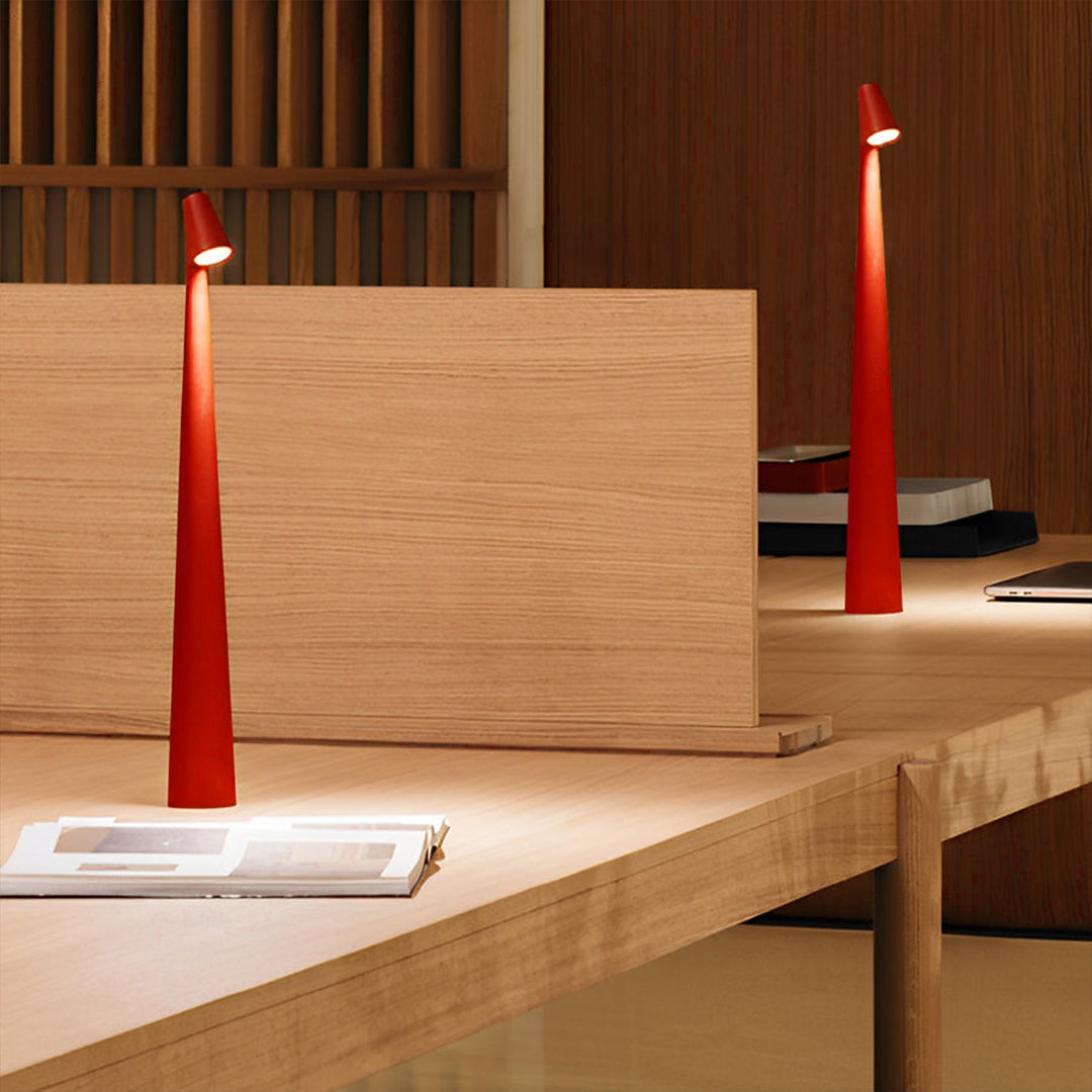 Red cone shaped table lamp used as accent lighting on a wooden display platform.