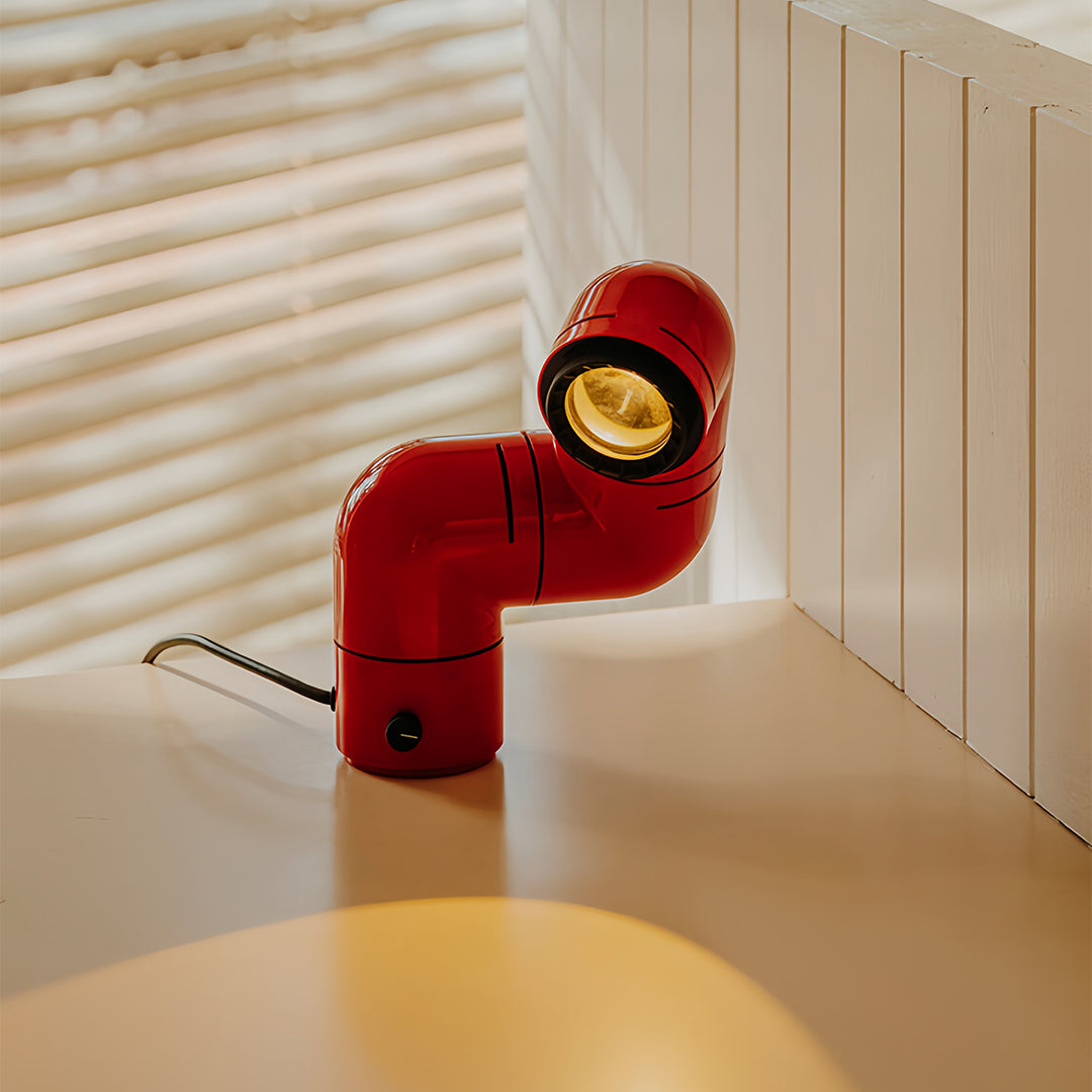 Vibrant red statement table lamp placed on a wooden surface under soft warm light.