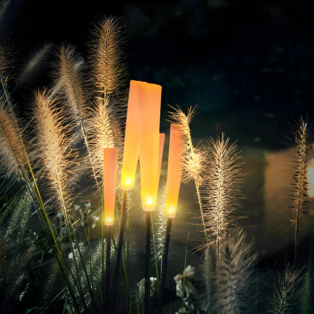Reed lights casting soft glow on decorative grasses in dark garden.