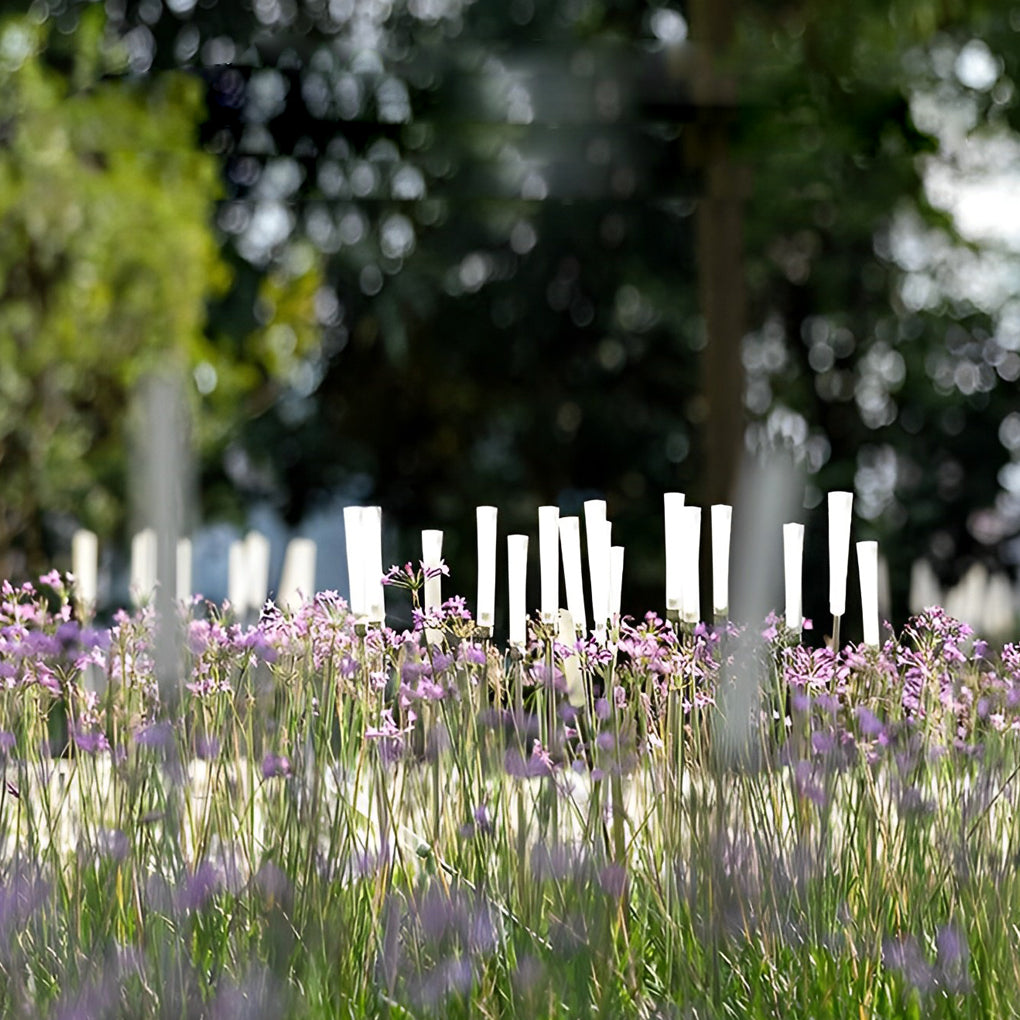 Reed lights casting warm glow on flower bed in evening garden.