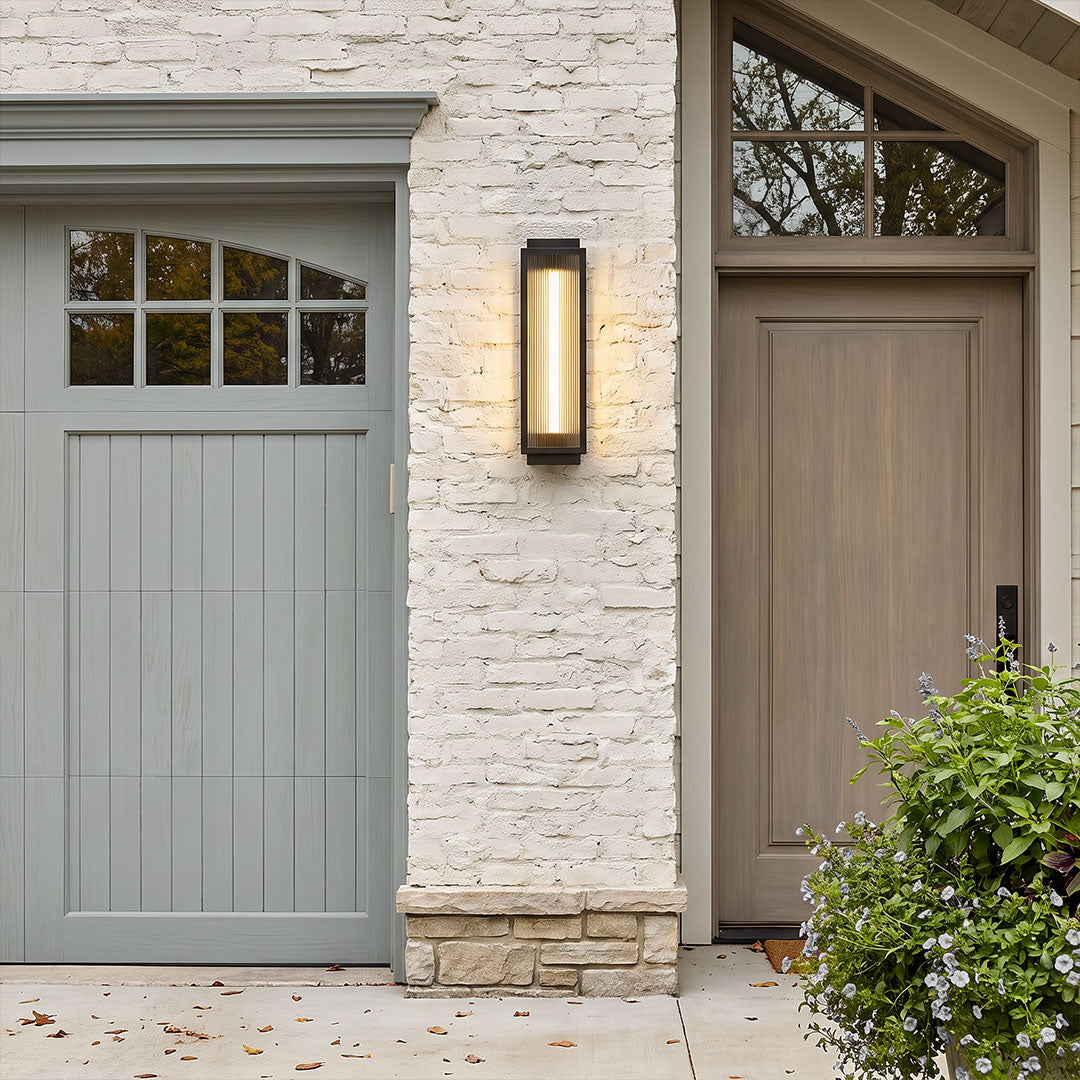 Reeded glass light installed beside a garage door and entryway, showcasing a tall modern wall fixture with warm ambient lighting.