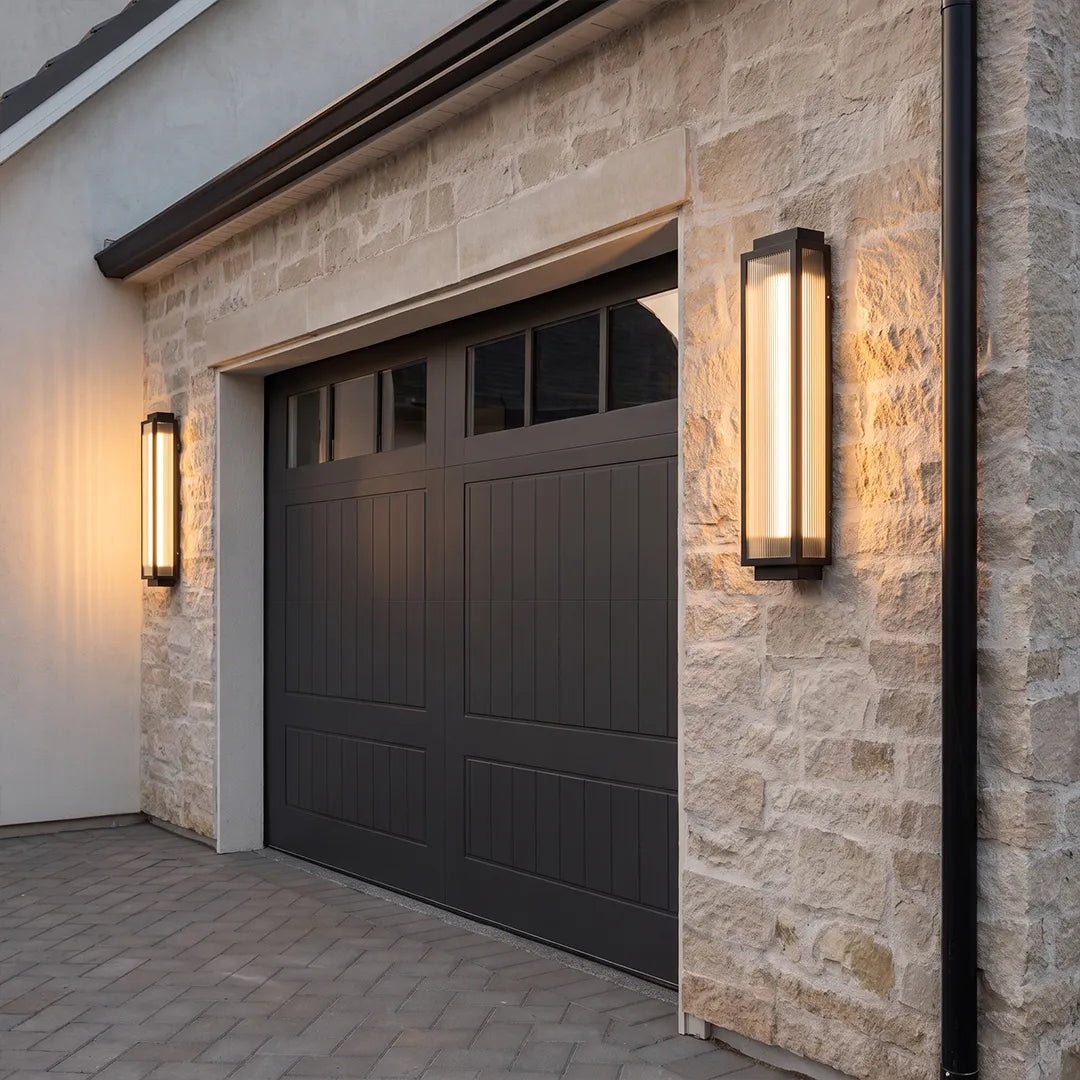Reeded glass light mounted on a stone exterior wall beside a black garage door.