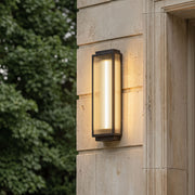 Reeded glass light mounted on a stone exterior wall, featuring a vertical rectangular frame and warm glowing illumination.
