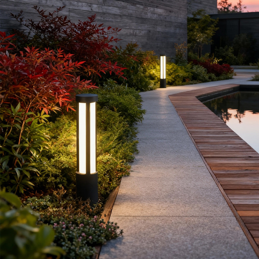 Residential bollard lights placed along a curved outdoor path near landscaping and water, providing soft illumination for safe nighttime walking.