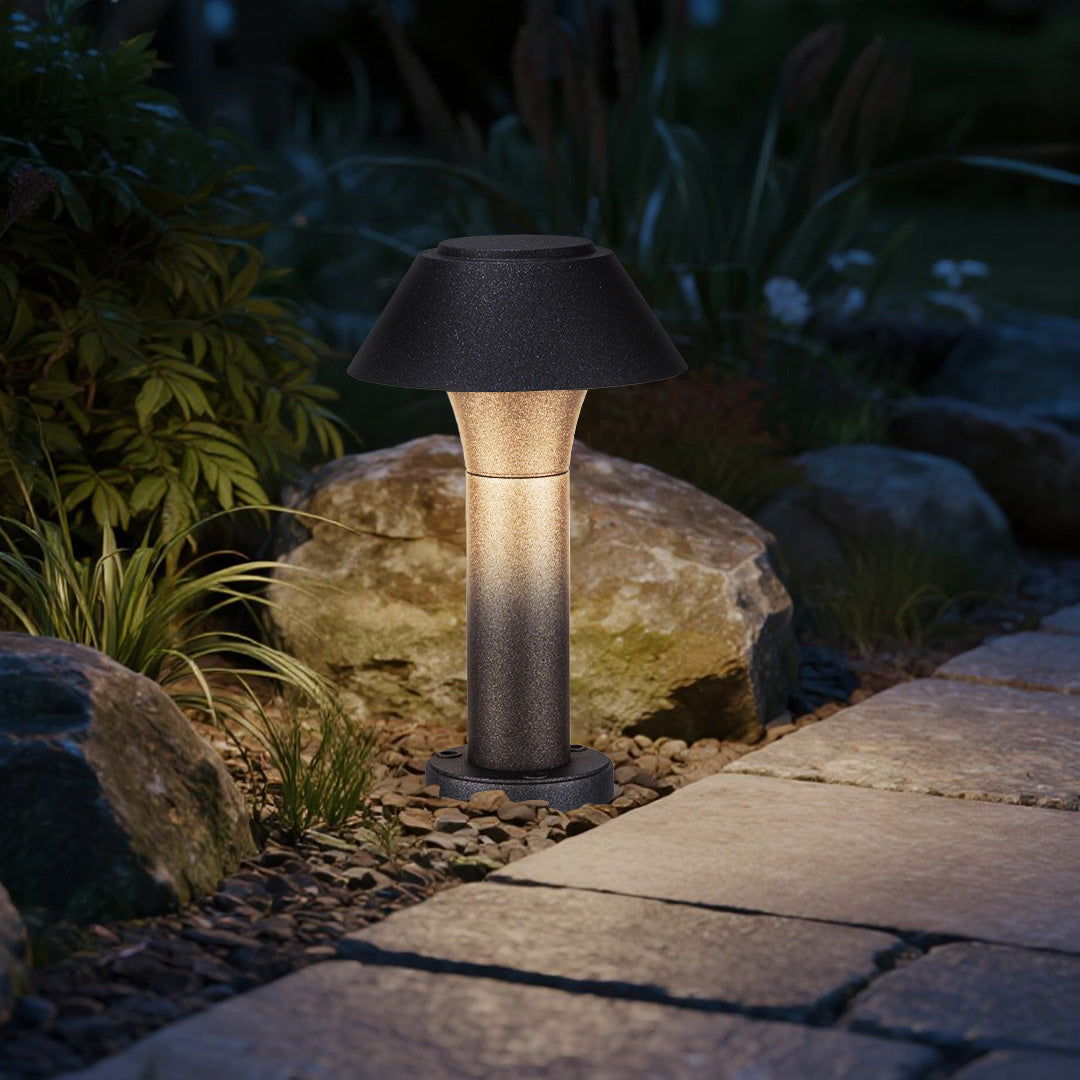 Residential bollard lights installed near stones and plants, creating focused illumination for a small garden pathway.