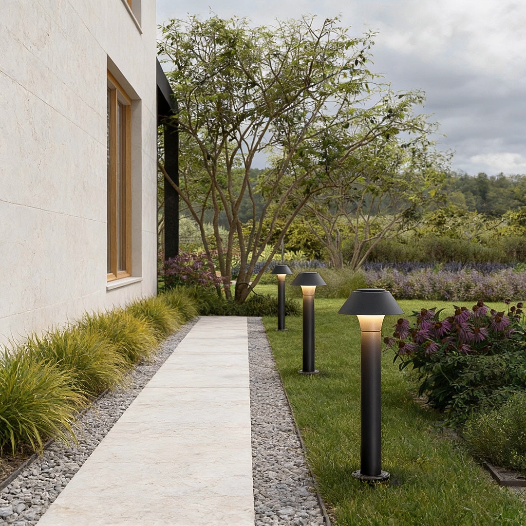 Residential bollard lights lining a straight concrete walkway beside a home, enhancing safety and visual appeal in the garden.