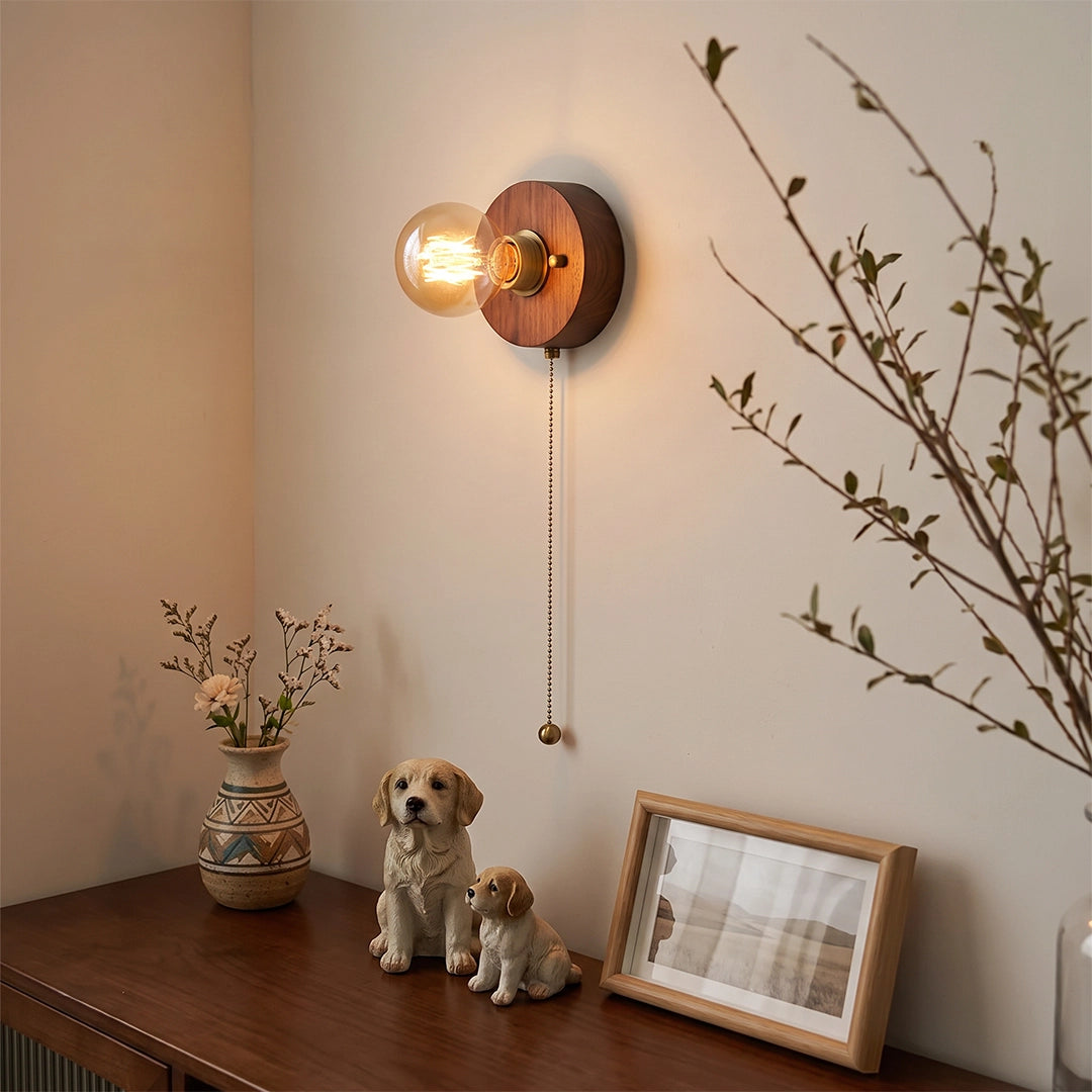 Retro bedside wall light with a pull chain mounted above a console table with small decor.