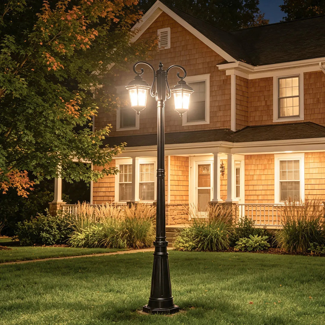 Retro outdoor lamp post installed on a front lawn in front of a traditional two-story house at night.