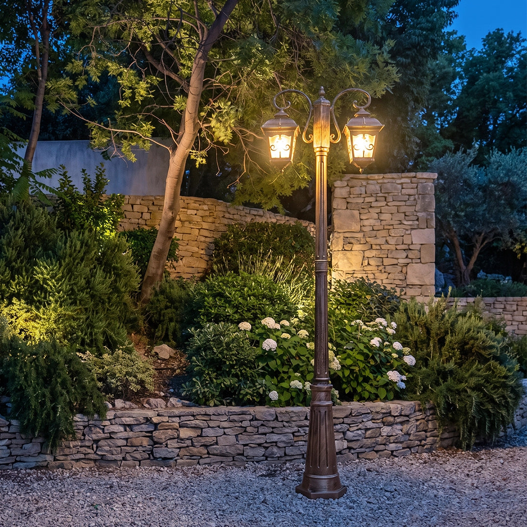 Retro outdoor lamp post illuminating a landscaped garden path, with dual lanterns casting a warm glow against stone walls and greenery.