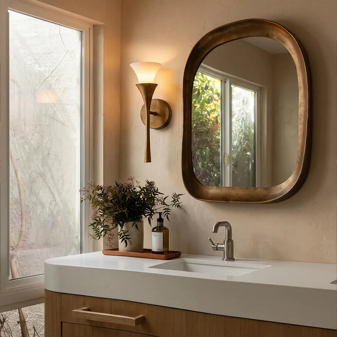 Retro wall sconce mounted beside a bathroom mirror with a warm brass finish and frosted shade.