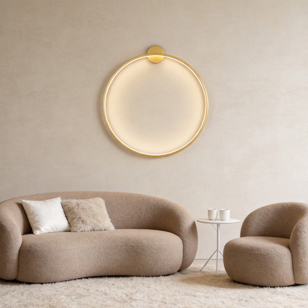 Ring wall lamp with gold finish, illuminating a cozy modern living room.