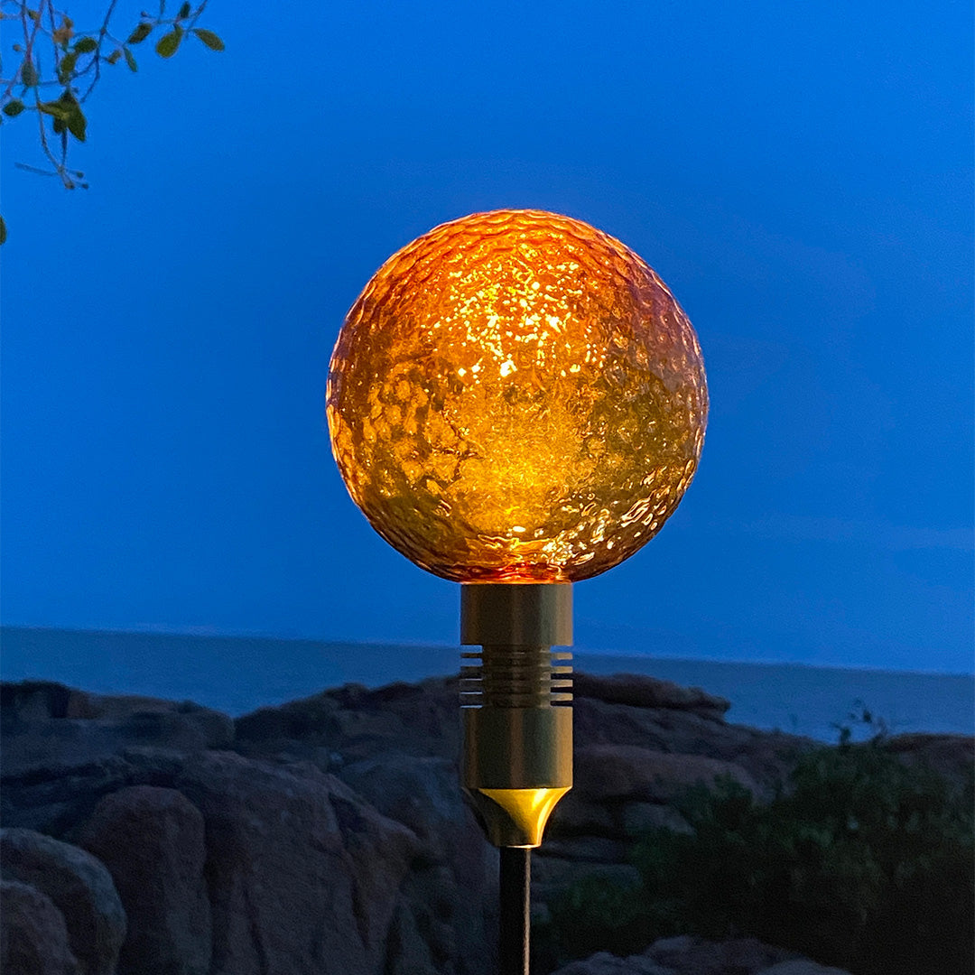 Warm amber crackle-glass globe light illuminating rocky landscaping for path landscape lighting.