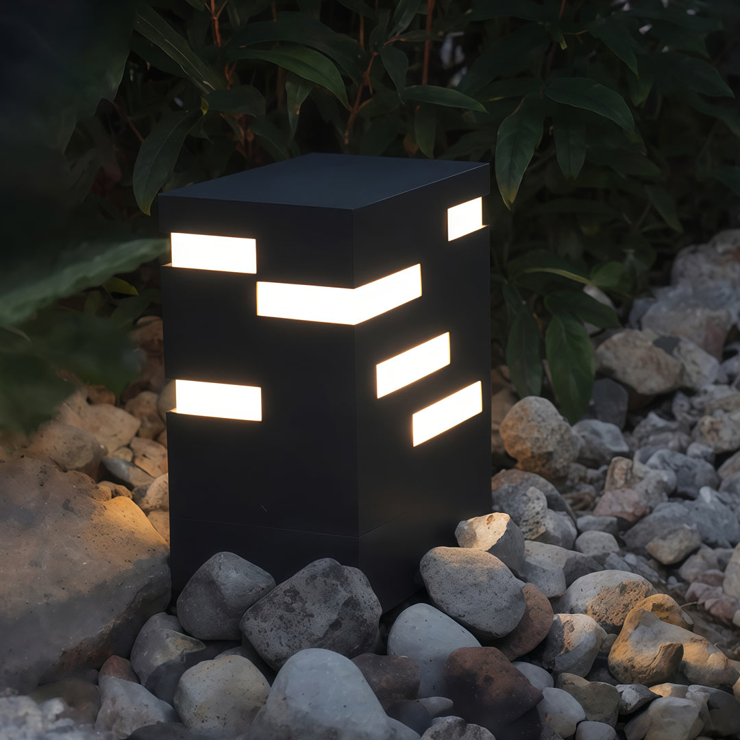 Modern black led bollard lights installed on rocky ground, providing structured horizontal glow for stylish evening illumination.