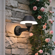 Modern black dome wall light with extending arm illuminating brick exterior wall at dusk