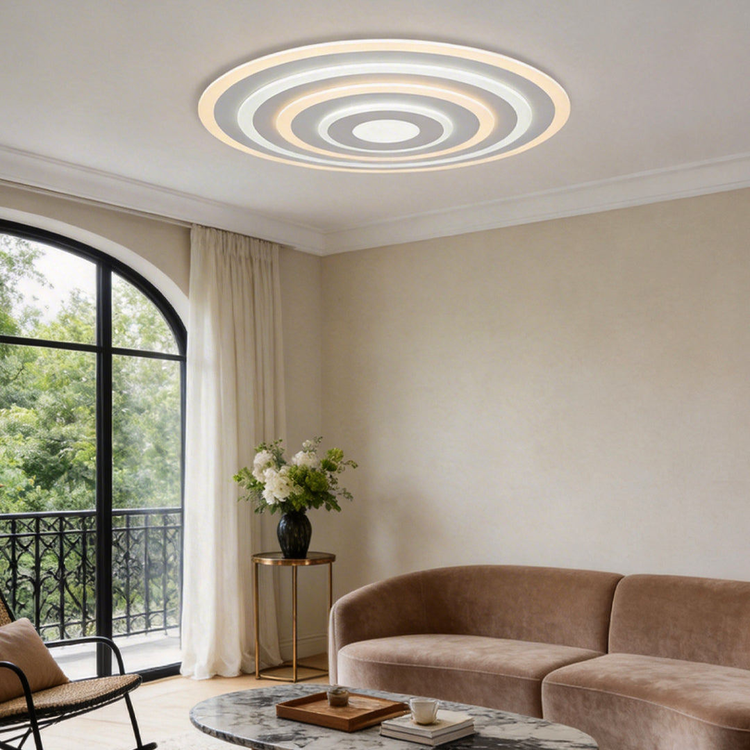 Round flush mount ceiling light providing soft illumination in a modern living room with large windows.
