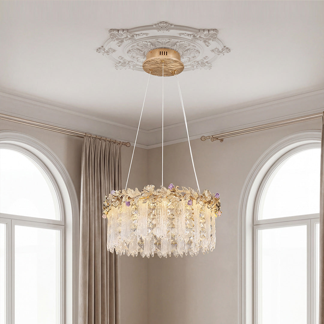 Stunning round gold chandelier crystal design featuring a botanical leaf band with subtle purple accents and cascading clear fringes, suspended from an ornate ceiling medallion.