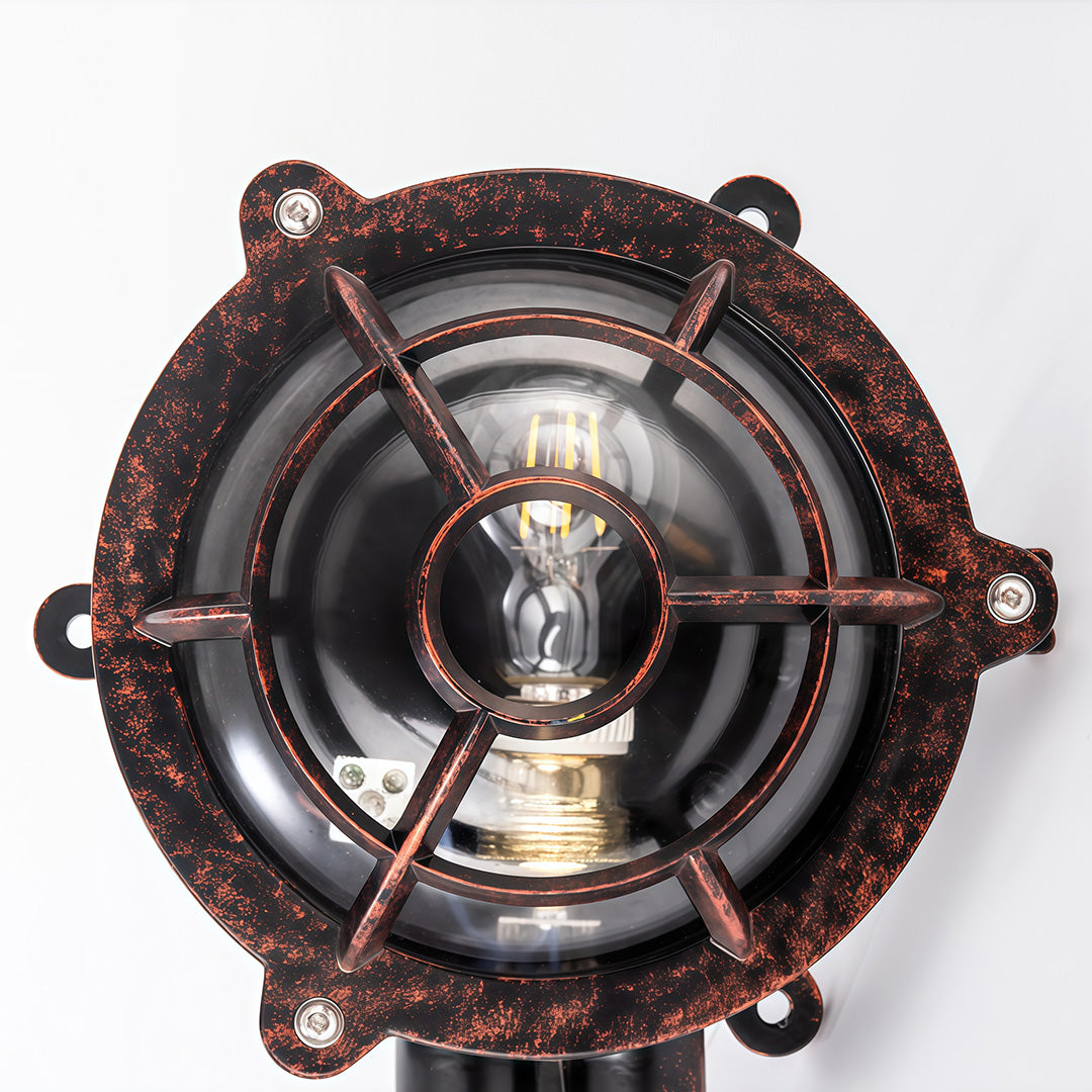 Round industrial outdoor sconce with ship-wheel inspired design showing aged bronze finish and clear glass