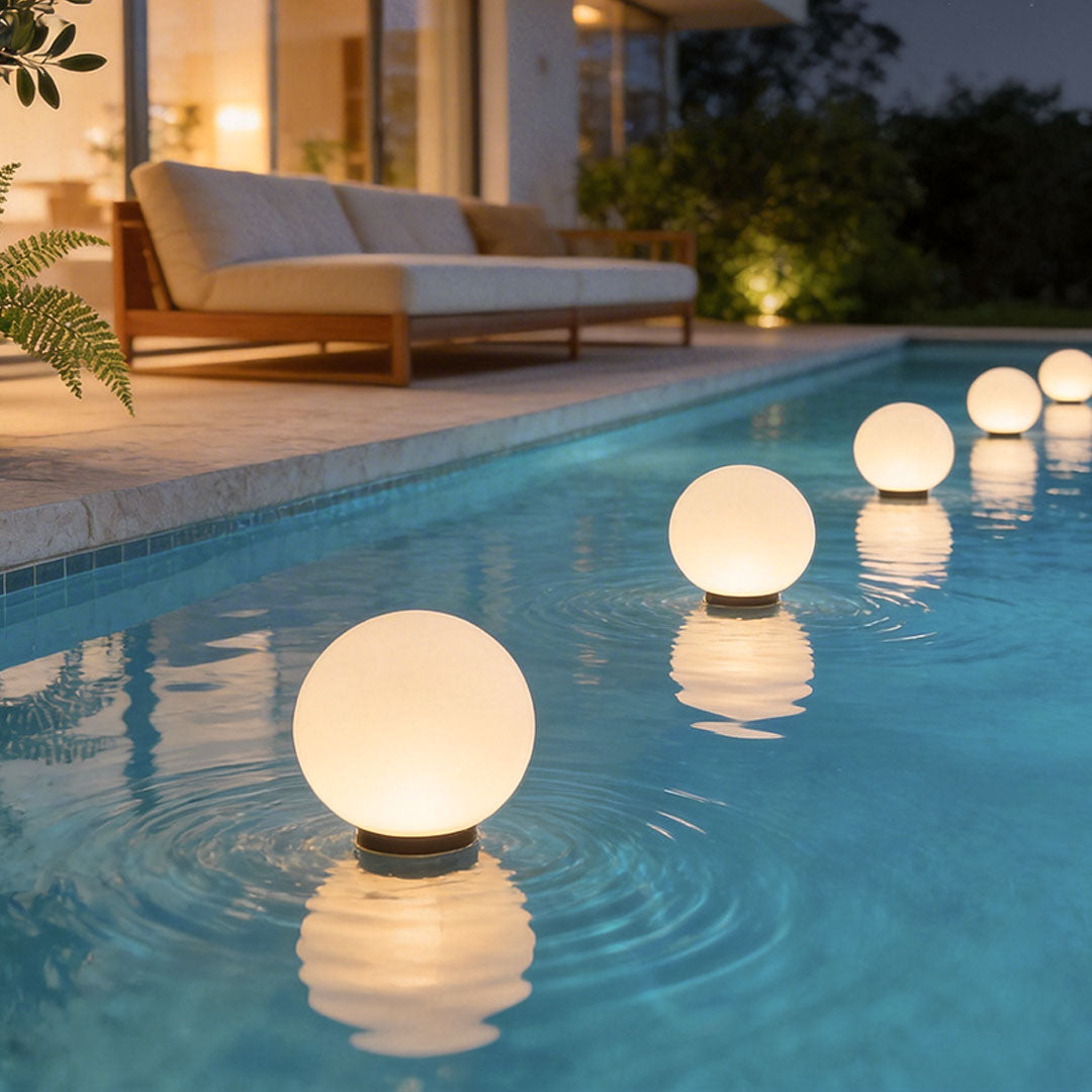 Round landscape lighting floating in a bright pool next to cozy outdoor sofa lounge chairs.