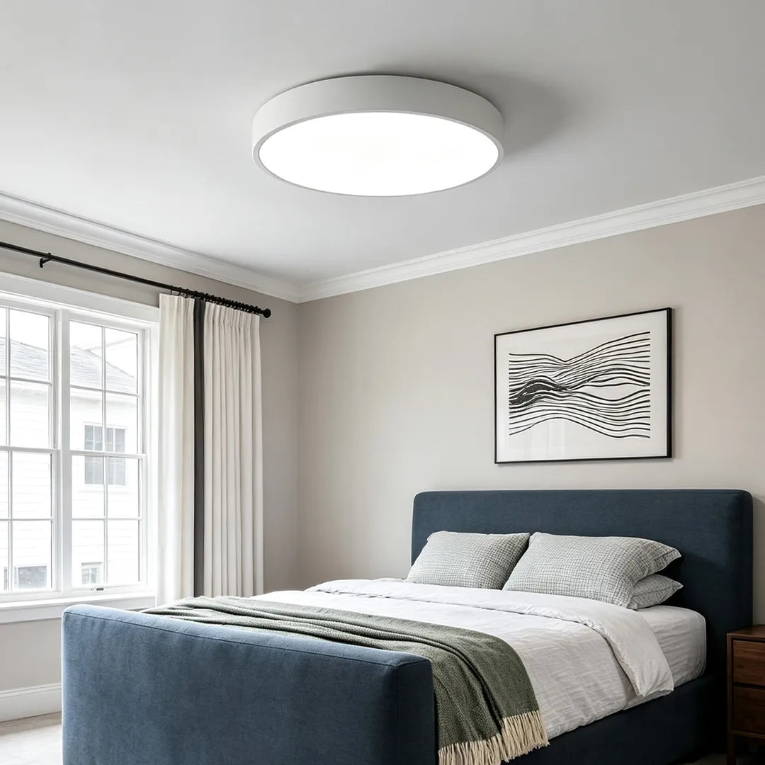 Round LED ceiling lights illuminating a bright bedroom with large windows, crown molding, and a dark upholstered bed.