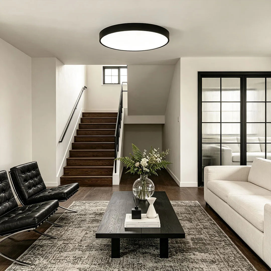 Round LED ceiling lights mounted in a bright living room with staircase, black framed doors, and modern furniture.