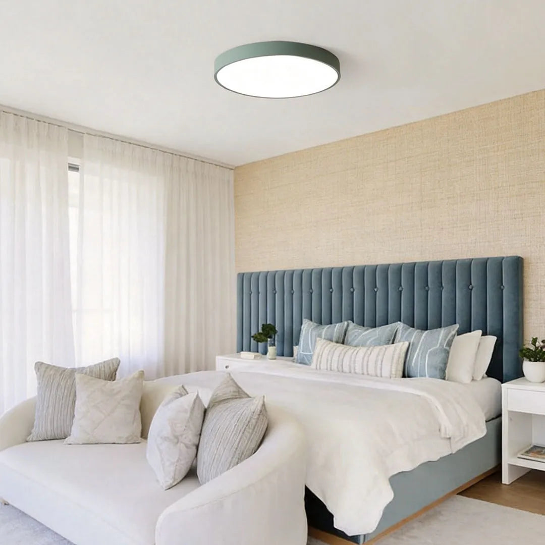 Round LED ceiling lights installed above a bedroom with a green upholstered headboard and soft neutral decor.
