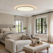 Round LED ceiling lights installed in a soft neutral bedroom with a cozy lounge chair and ottoman.