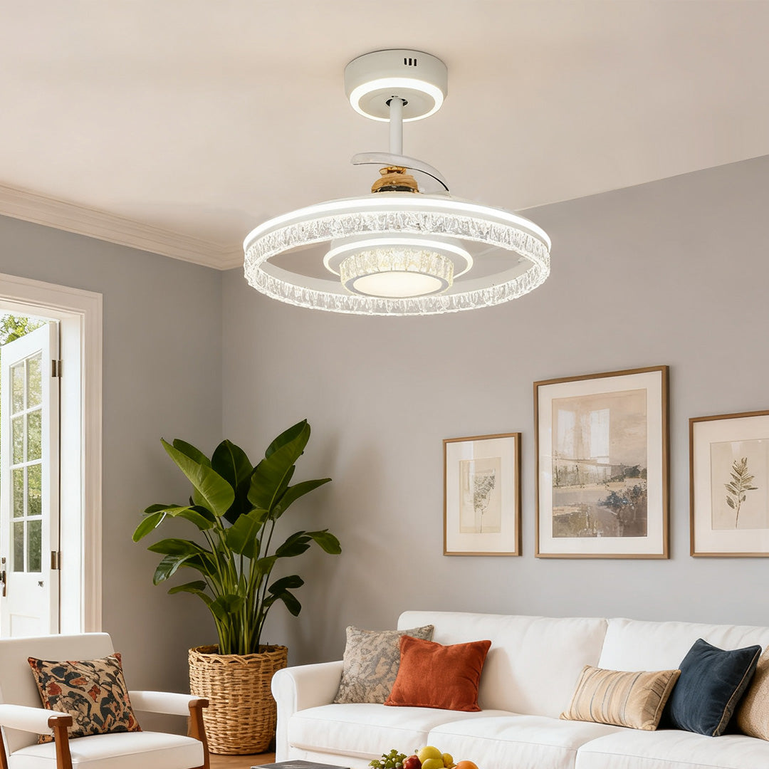 Ceiling fan with round light fixture and crystal design illuminating a living space with a large houseplant and glass double doors. 