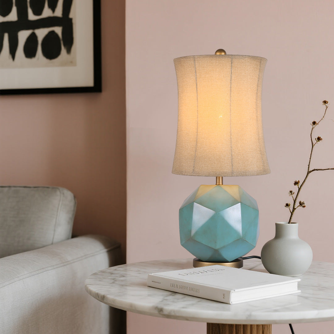 The modern industrial table lamps on a round white marble side table, casting a warm glow in a minimalist pink and white living room setting.