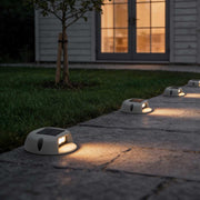 Round outdoor deck light illuminating a garden pathway with warm ambient glow.