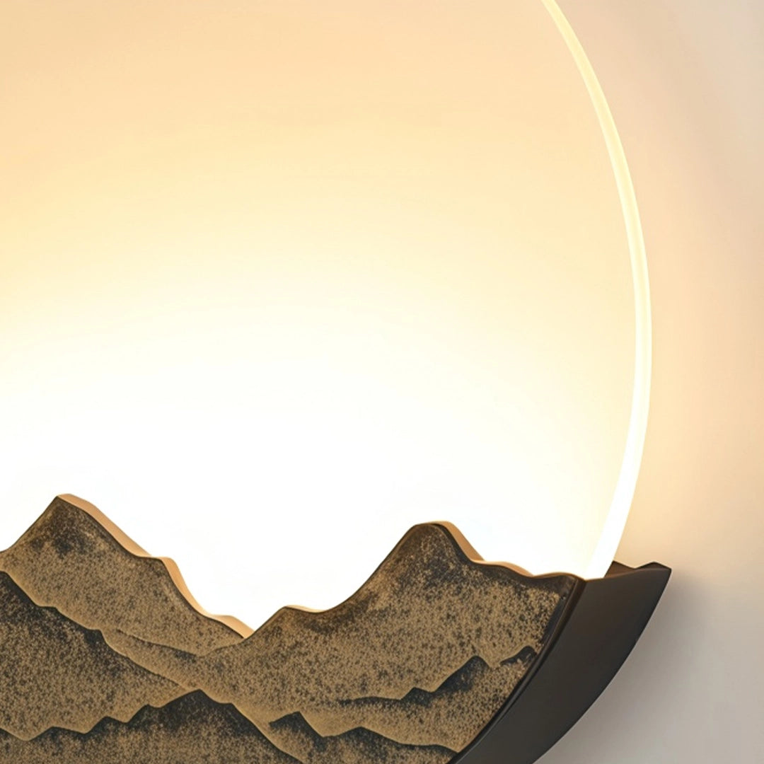 Close-up of a round outdoor sconce with warm backlight and textured mountain detail.