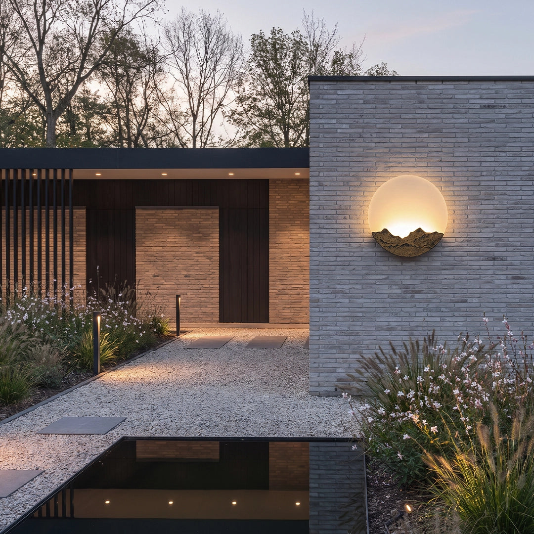 Round outdoor sconce installed on a stone entry wall in a modern outdoor space at dusk.