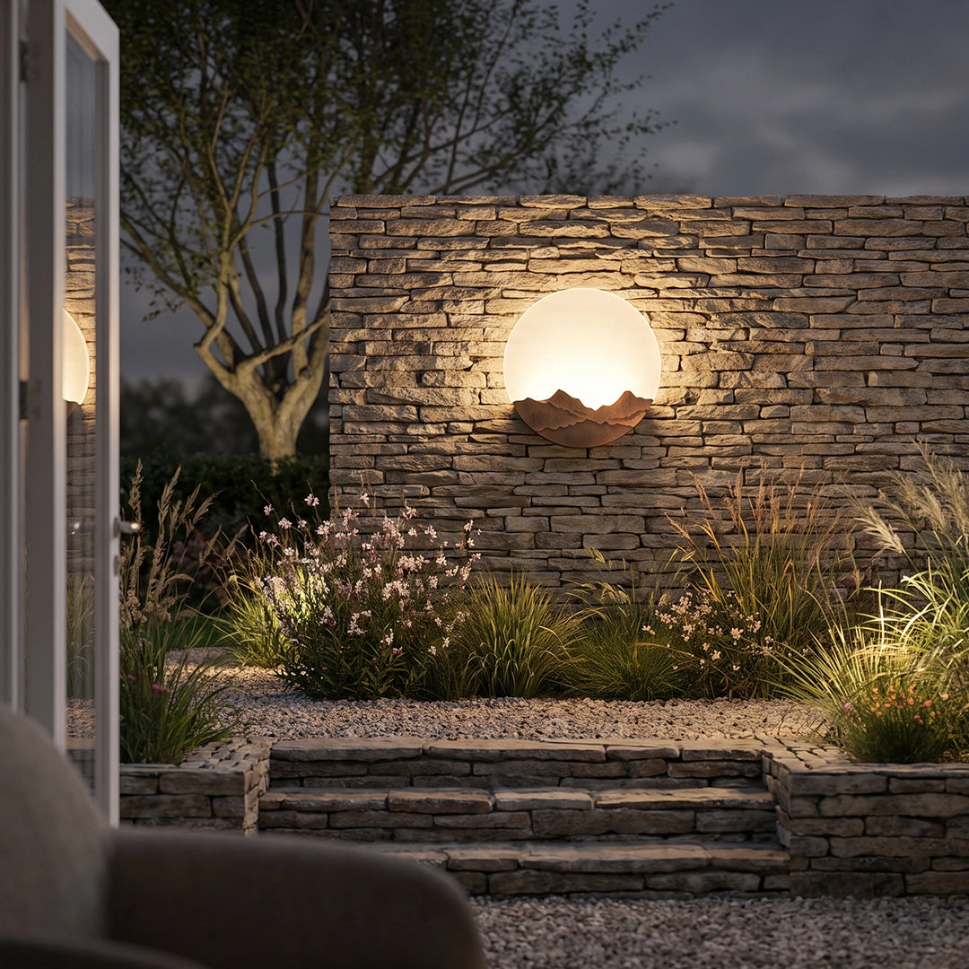 Round outdoor sconce illuminating a stone wall and garden steps at night.