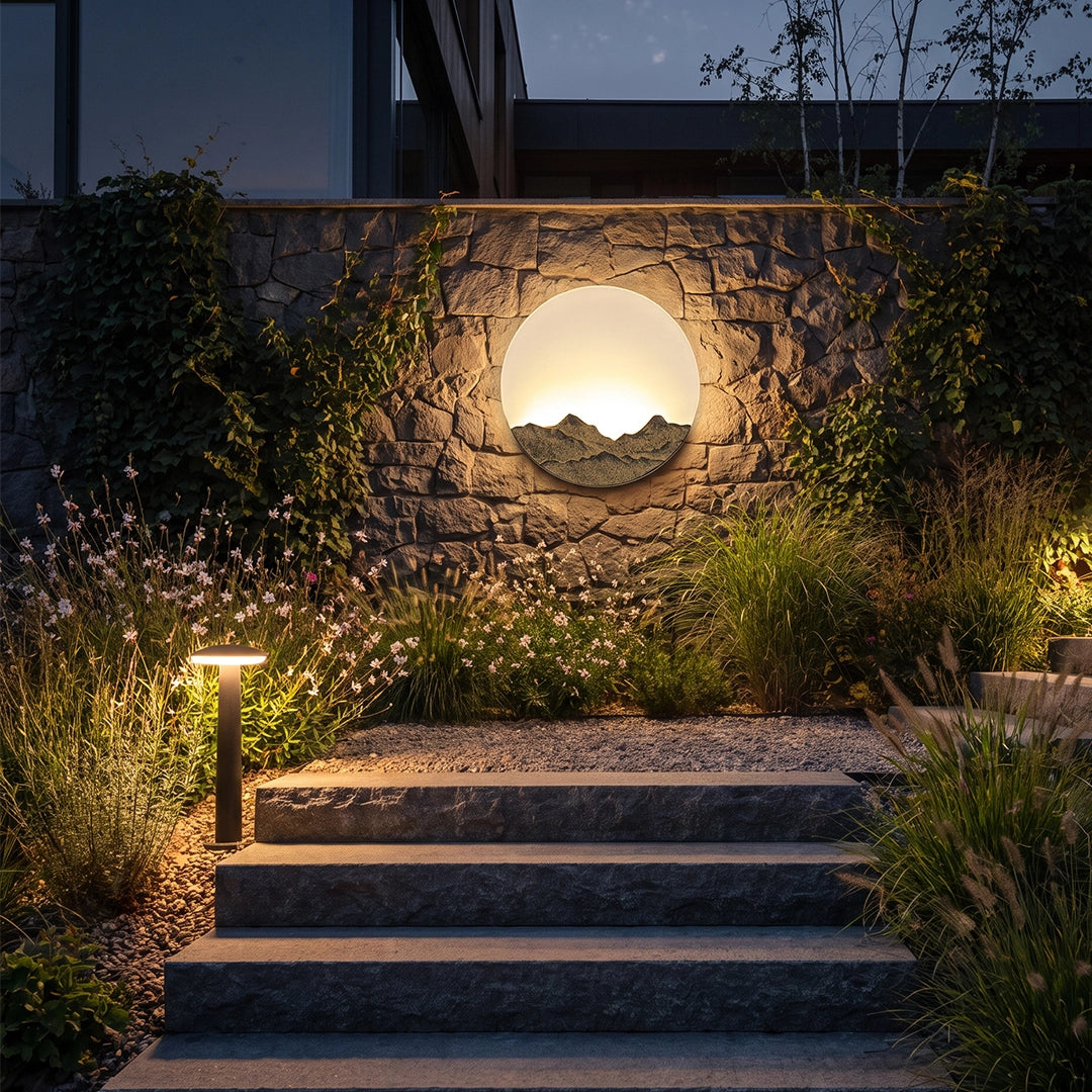 Round outdoor sconce lighting a landscaped stone wall and steps at night.