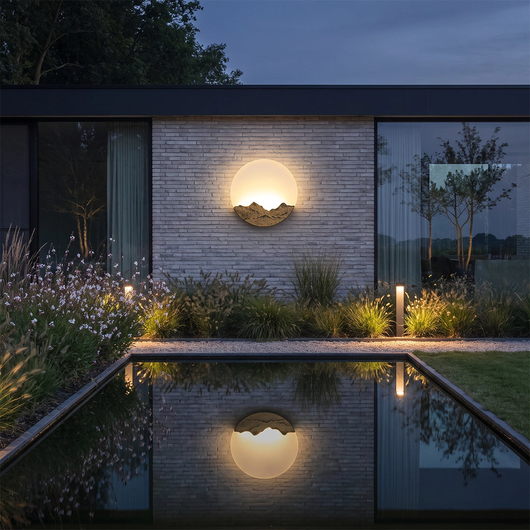 Round outdoor sconce beside a pool, reflecting on the water in a modern courtyard.