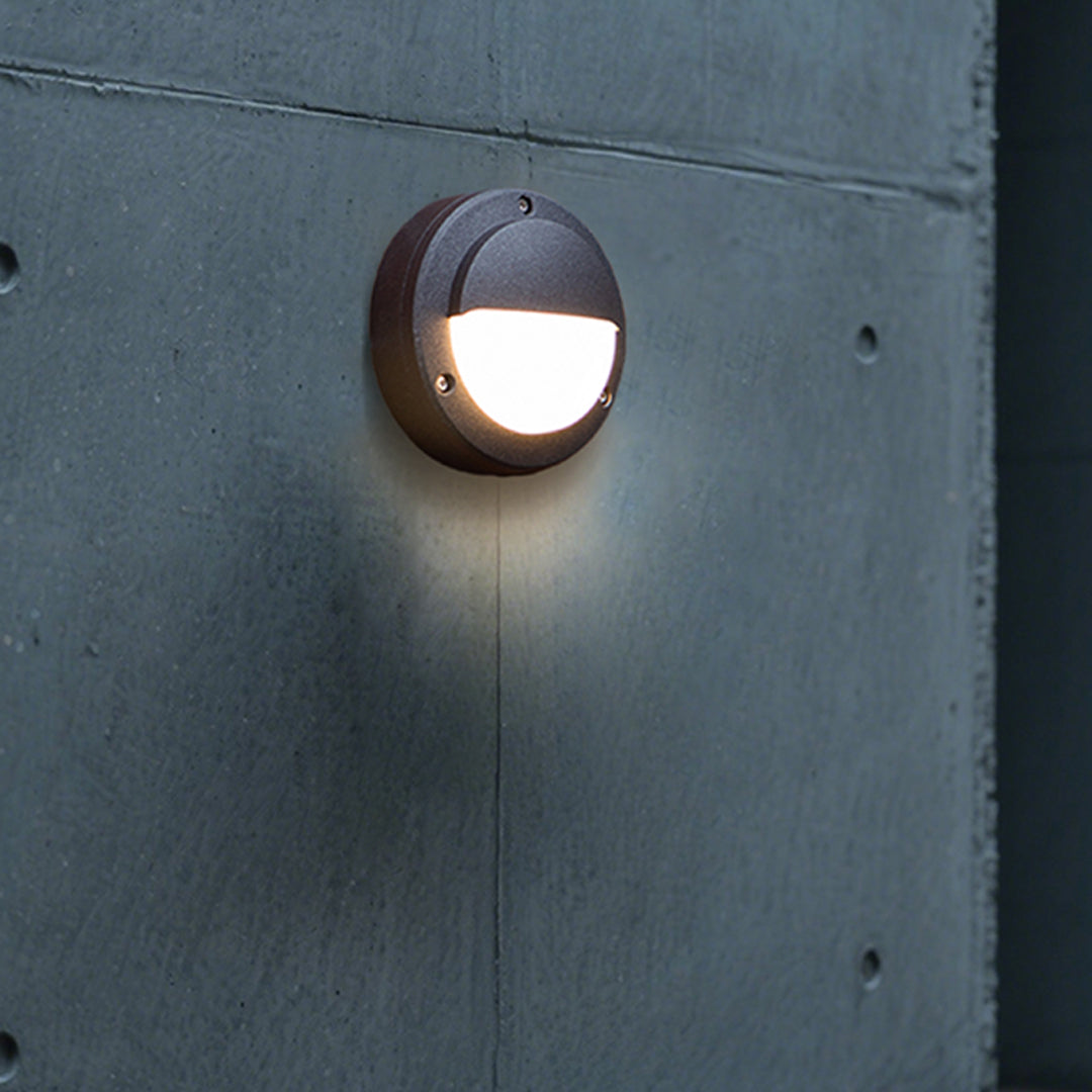 Round outdoor wall sconce providing ambient lighting on blue-grey exterior surface