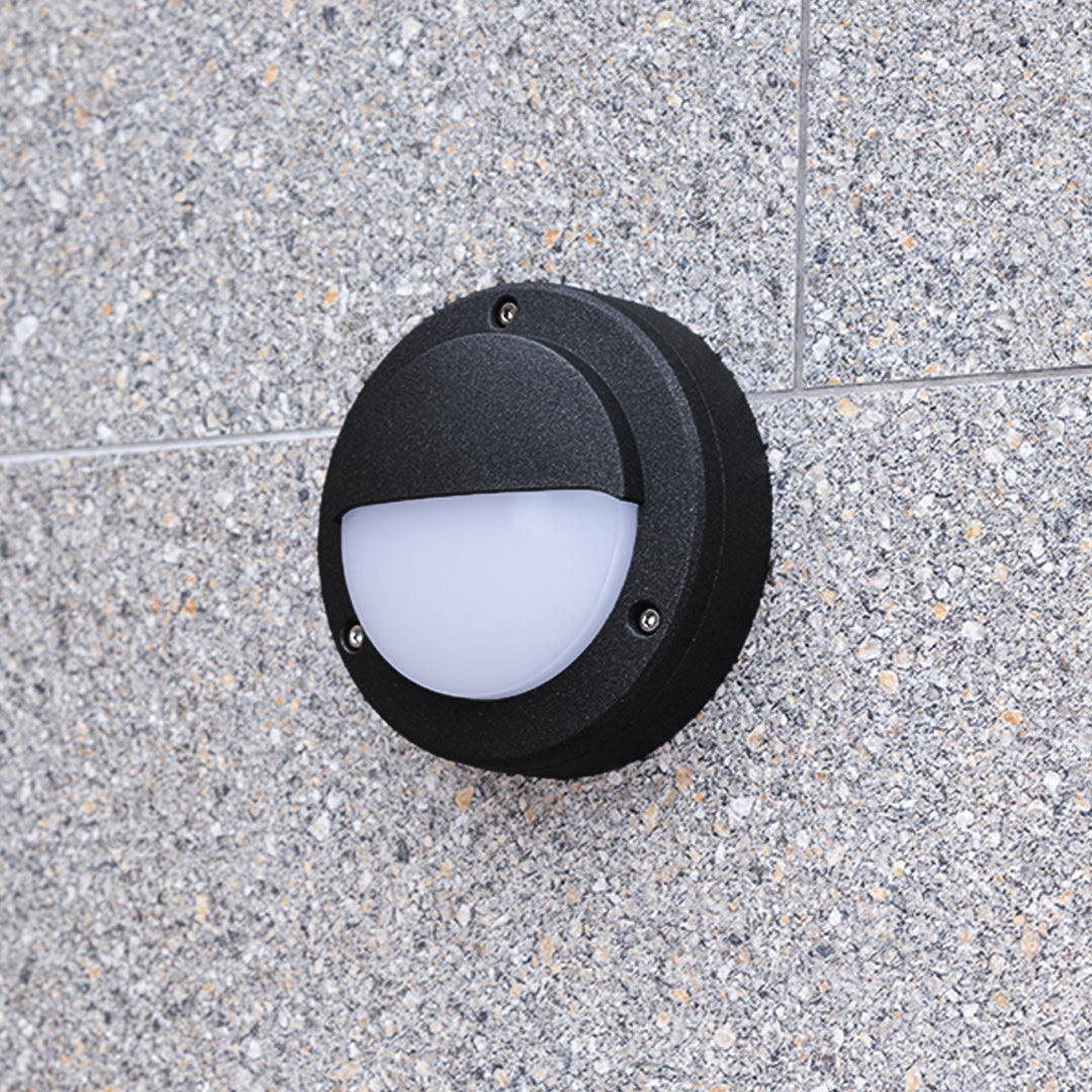 Round outdoor wall sconce with eyelid design installed on textured grey concrete
