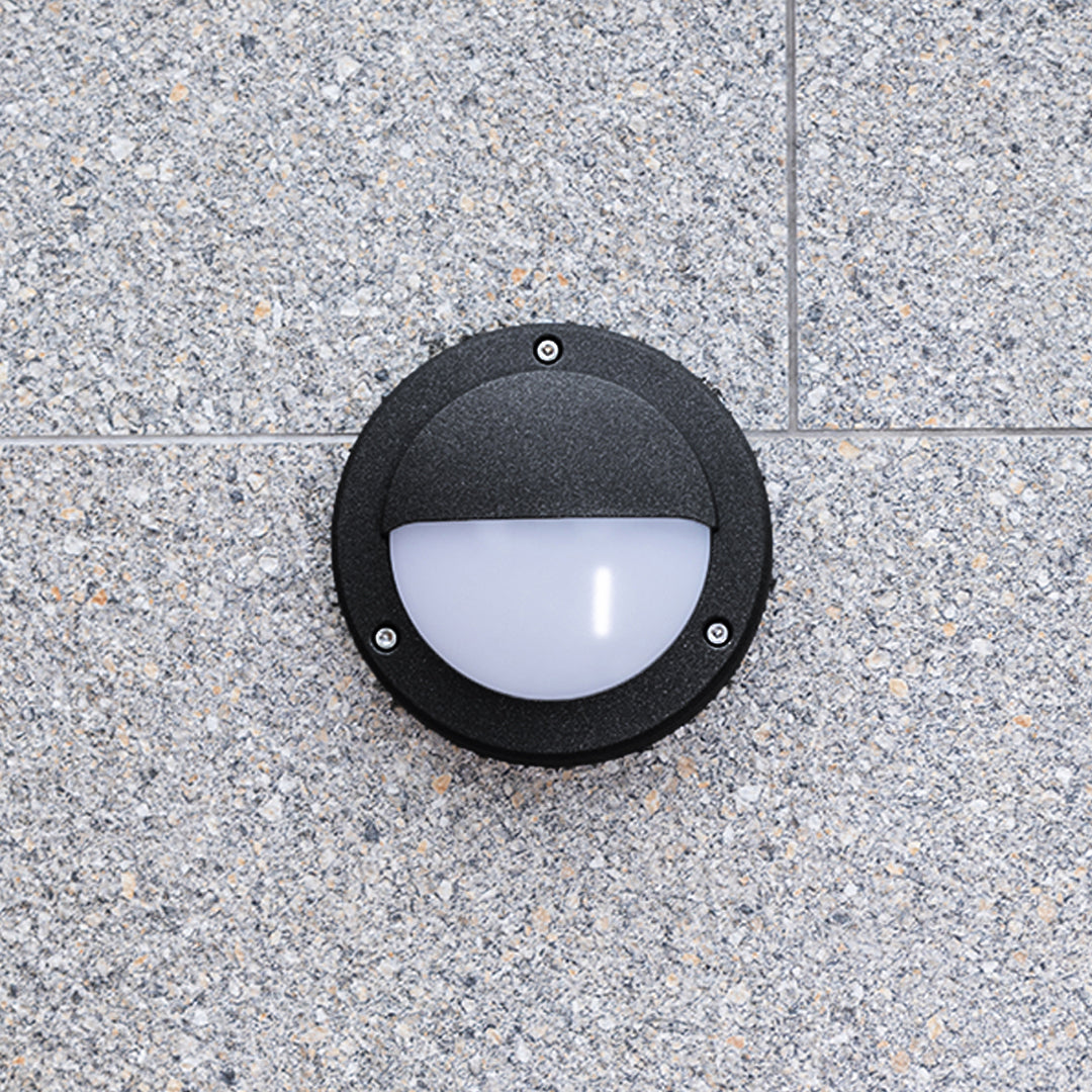 Round outdoor wall sconce mounted on grey granite creating downward illumination