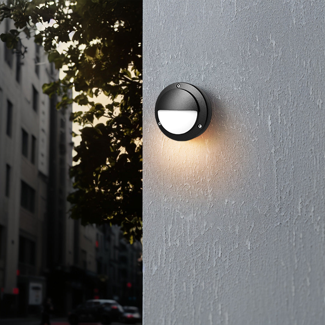 Round outdoor wall sconce brightening grey wall in modern outdoor setting at dusk