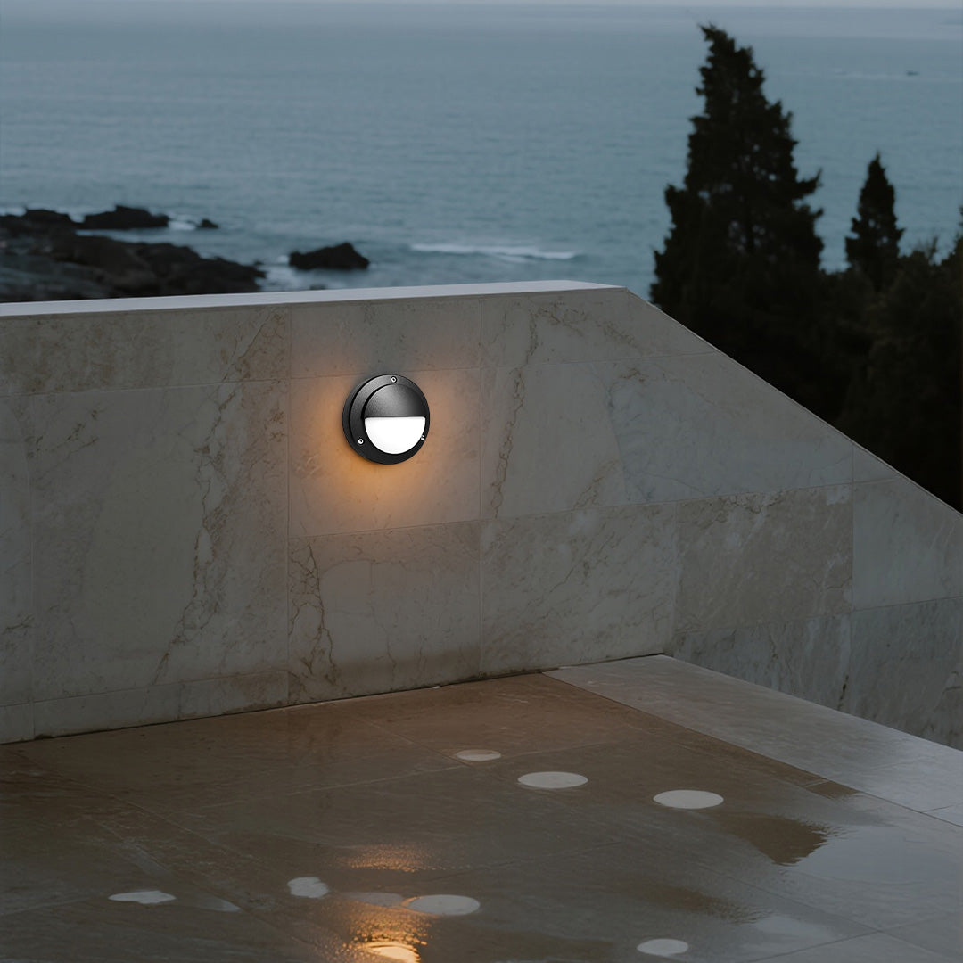 Round outdoor wall sconce casting warm glow on beige exterior wall at evening