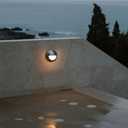 Round outdoor wall sconce casting warm glow on beige exterior wall at evening
