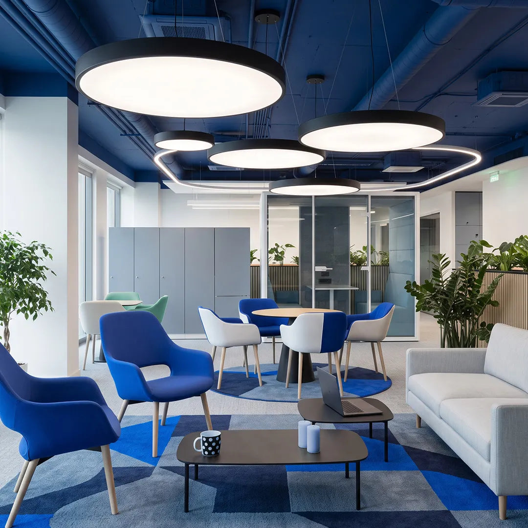 Round pendant lights hanging in a bright office lounge with blue seating and layered circular ceiling fixtures.
