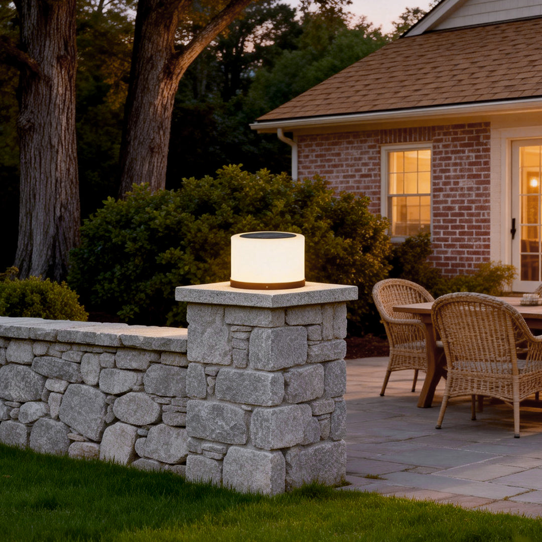 Round pillar lights illuminating a stone wall in a cozy backyard setting.
