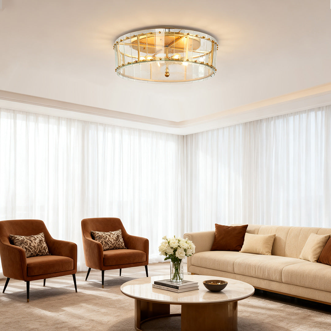 Round flush mount gold light providing soft ambient illumination in a cozy sitting area with rich brown velvet armchairs and sheer white curtains.