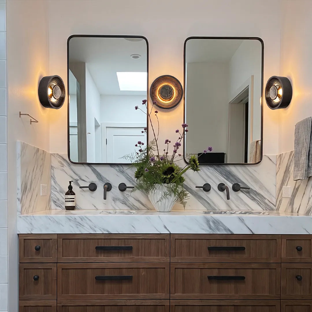 Round wall sconce pair flanking bathroom mirrors above a double vanity with marble countertops.