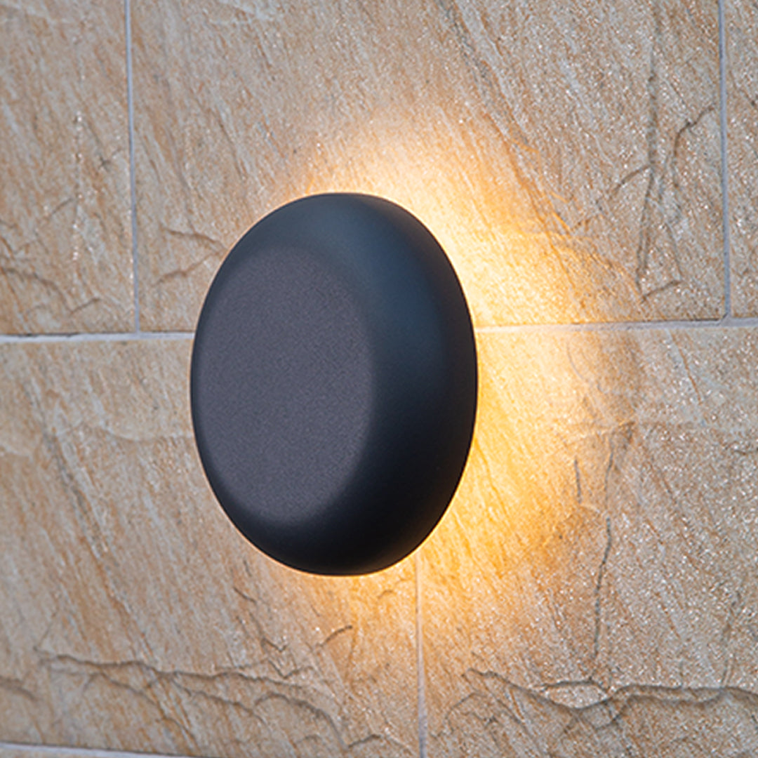 Round waterproof outdoor wall light casting warm halo illumination on beige textured stone surface