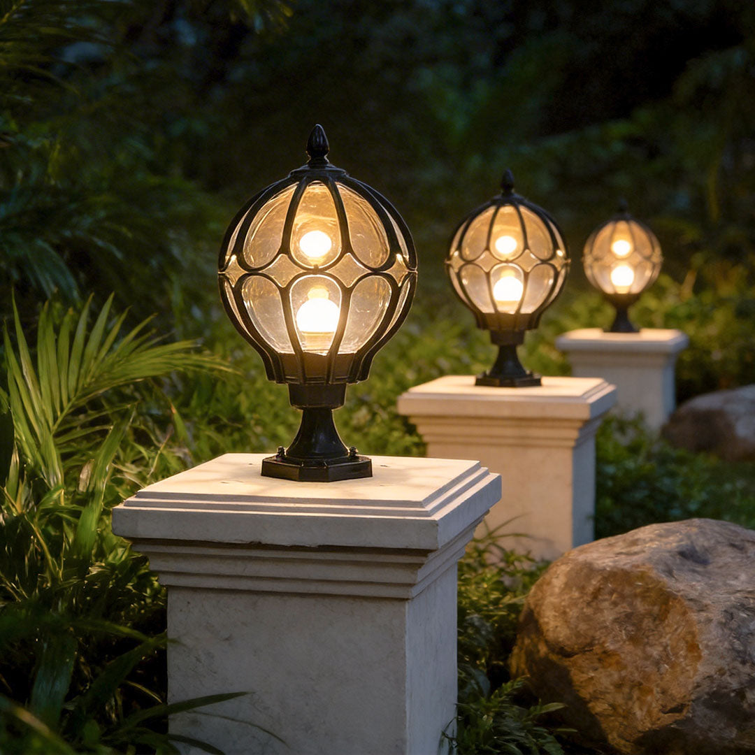 Row of black globe pillar lights on stone pedestals illuminating a garden path at night time.