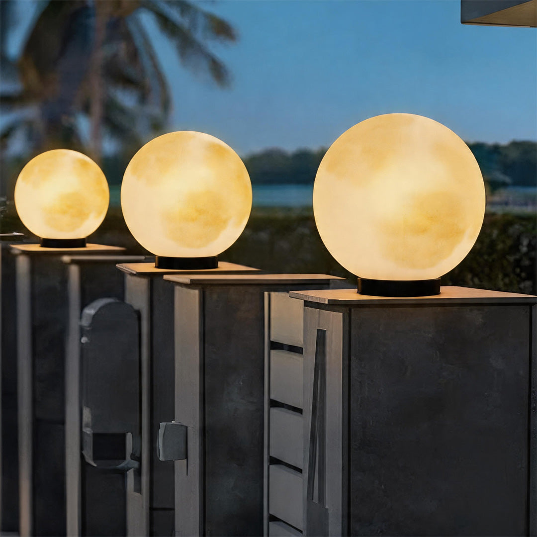 Row of glowing moon pillar lights illuminating a modern dark grey fence during the nighttime.