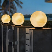 Row of glowing moon pillar lights illuminating a modern dark grey fence during the nighttime.
