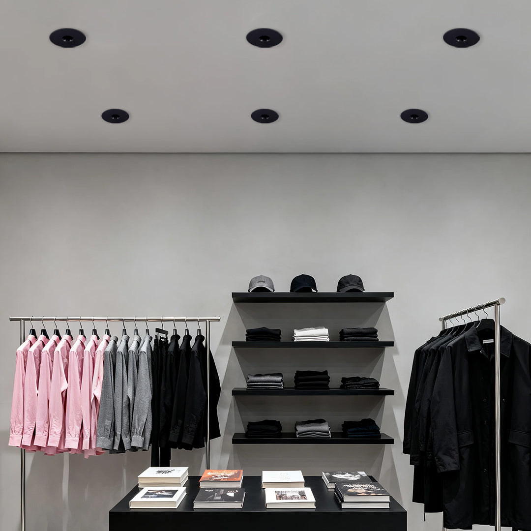 Row of LED recessed spotlights brightening minimalist retail space with clothing displays and shelving