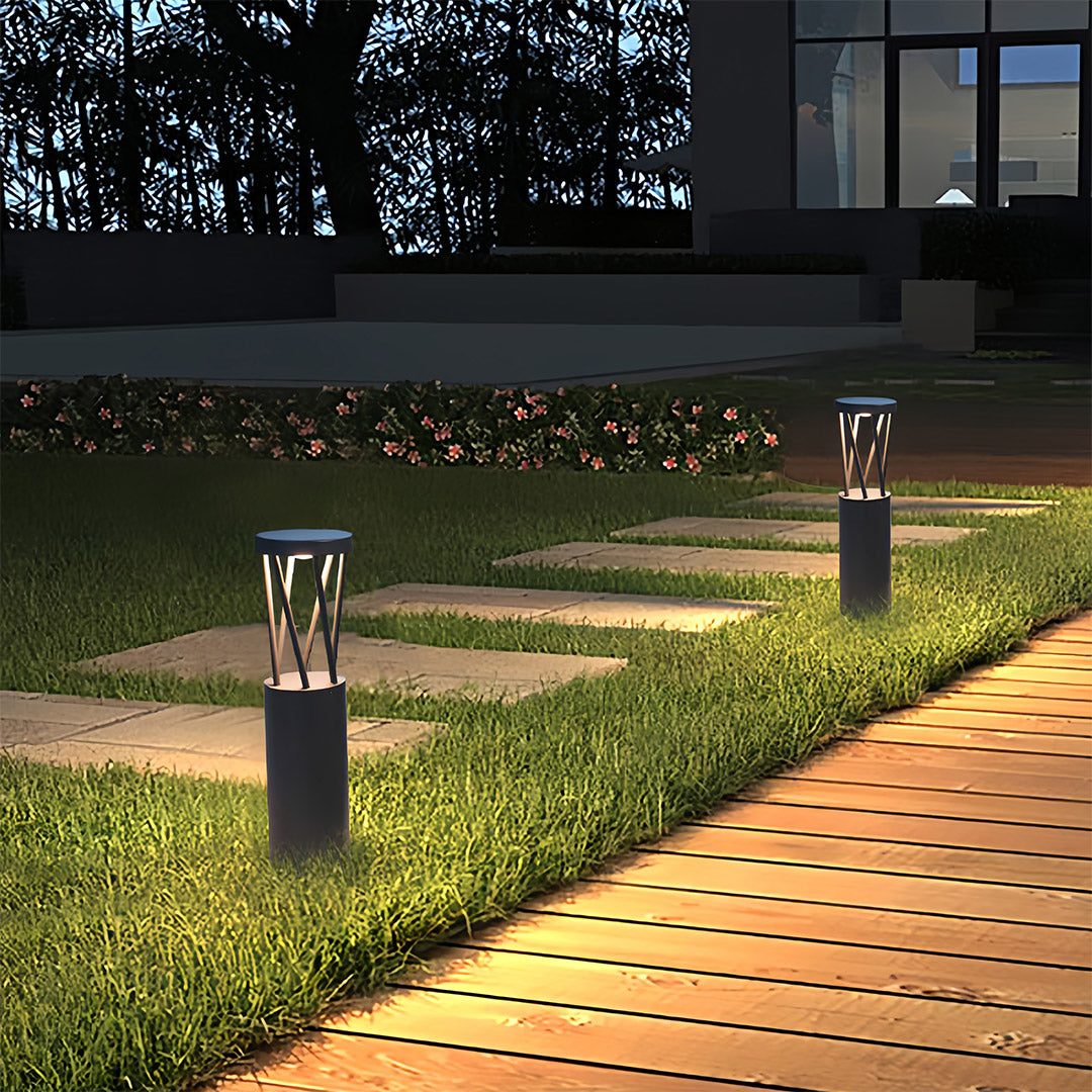 Row of modern black mushroom cap bright path lights illuminating a stone walkway and lush green grass at night.